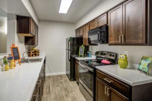 Well lit kitchen with oven, microwave, refrigerator, dual sink, wood toned vinyl floor, dark brown drawers and cabinets