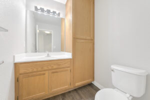Interior Unit Bathroom, white walls, light brown cabinetry, white countertop, vanity mirror, wood like floors.