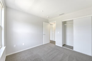 Interior Unit Bedroom, Gray Carpeting, sliding closet door, wood like floors in hallway, white walls.