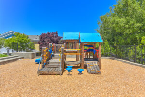 Exterior Playscape, soft landing ground, partially fenced, trees surrounding playground, photo taken on a sunny day