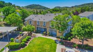 Aerial Exterior, covered parking, meticulous landscaping, trees scattered across property, photo taken on a sunny day.